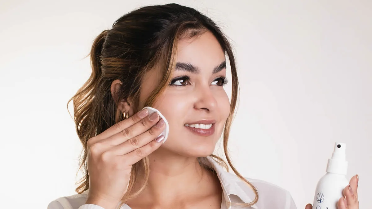 Mulher sorridente aplicando a Água Micelar da Loa Cosméticos no rosto com um algodão para manter a pele do rosto hidratada.